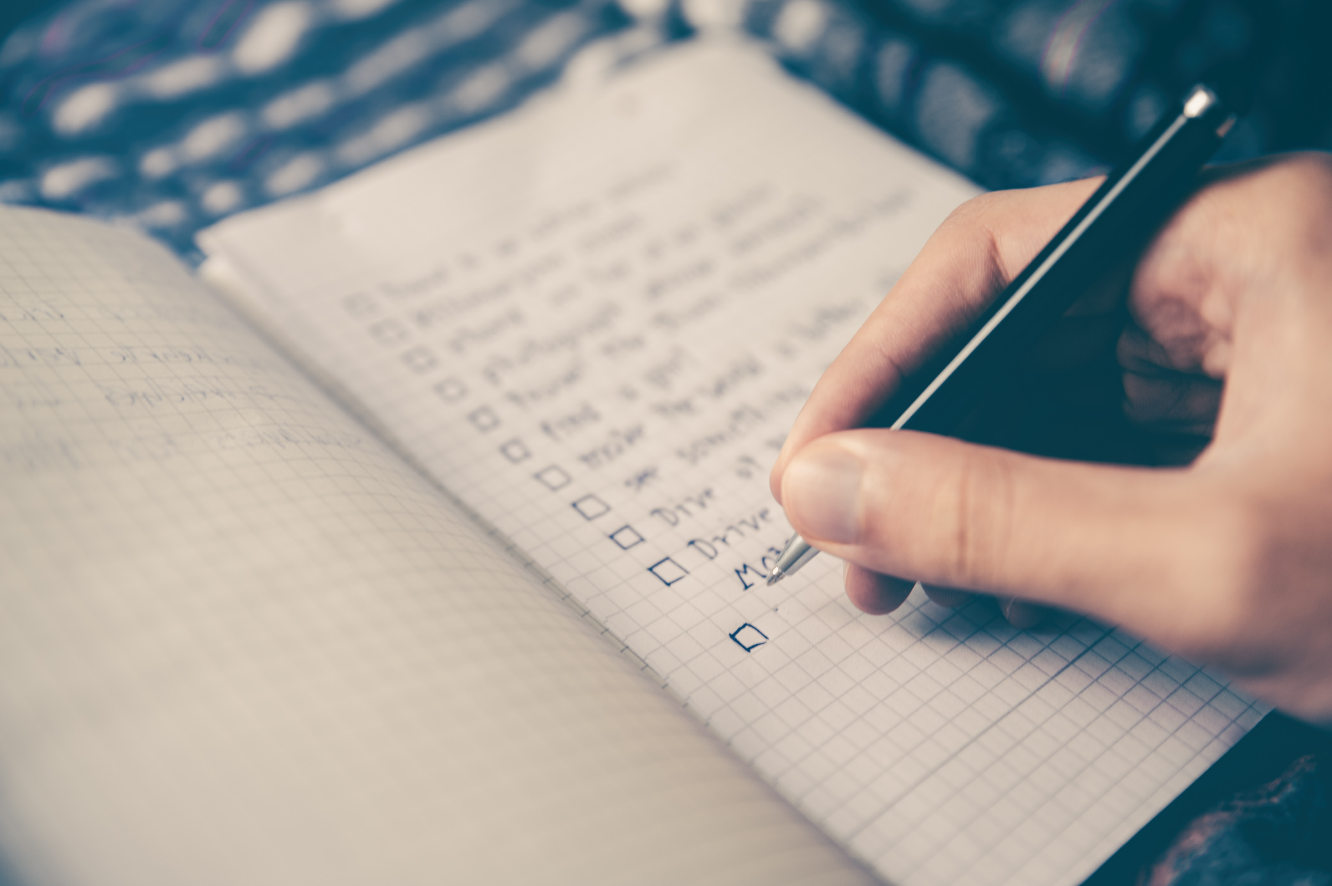 Hand holding a pen and writing notes on a notepad.